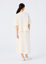 A woman with long dark hair in a low ponytail, wearing the SURPRISE BOX PRINT CAULIFLOWER set from me ISSEY MIYAKE and white sneakers, stands facing away against a plain light background.