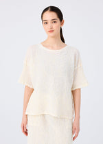 A woman with long dark hair tied back wears the SURPRISE BOX PRINT CAULIFLOWER set by me ISSEY MIYAKE, featuring a loose, textured cream cotton short-sleeved top and matching skirt, against a plain light background.