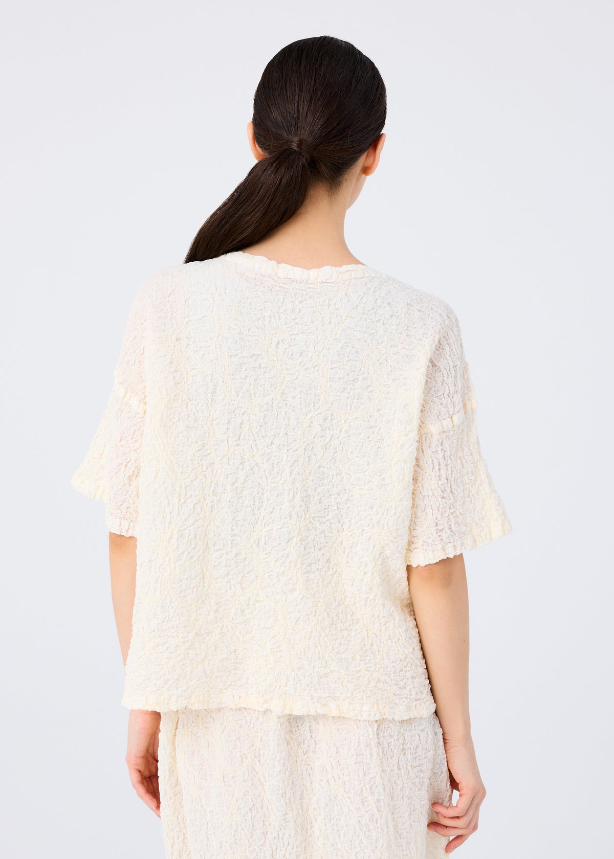 A woman with long dark hair in a low ponytail is seen from behind, wearing the me ISSEY MIYAKE SURPRISE BOX PRINT CAULIFLOWER set against a plain light background. view 6 of 7
