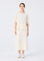 A woman stands facing forward in a loose-fitting SURPRISE BOX PRINT CAULIFLOWER top and matching midi skirt by me ISSEY MIYAKE, both in textured cream fabric. Her hair is pulled back, with white slip-on shoes against a plain white background.