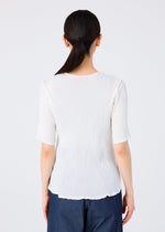 A person with long dark hair in a low ponytail is seen from behind, wearing the SEE-THROUGH CREPE COLOR white top by me ISSEY MIYAKE and dark blue pants, standing against a plain light background.