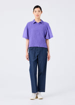 A person stands facing forward in a me ISSEY MIYAKE SHEER CAULIFLOWER lavender short-sleeved top, dark blue trousers, and white shoes against a plain white background.