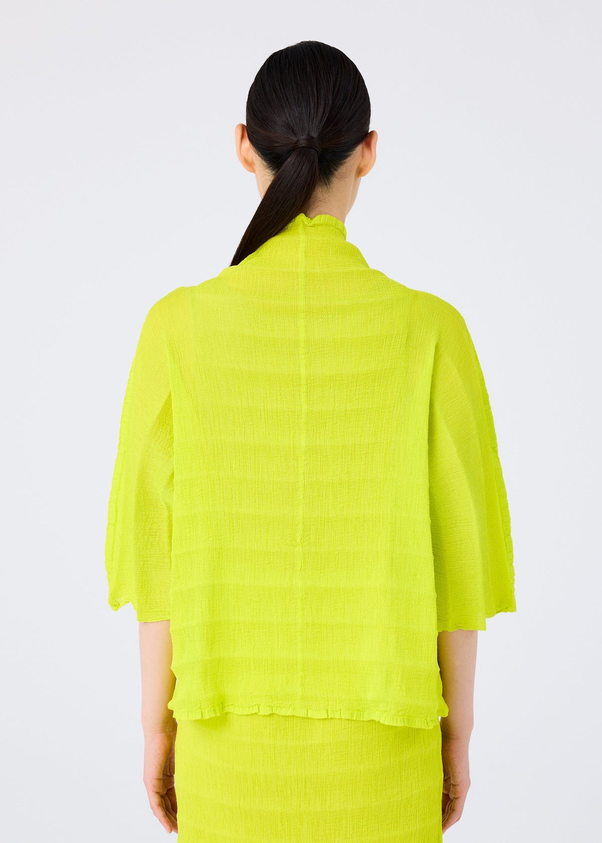 A person with long dark hair in a low ponytail is seen from behind, wearing the me ISSEY MIYAKE RIPPLE SEE-THROUGH CREPE top and matching skirt in bright yellow against a plain white background. view 6 of 7