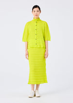 A woman with short dark hair wears the me ISSEY MIYAKE RIPPLE SEE-THROUGH CREPE, a bright yellow-green garment-dyed blouse with black buttons and a matching midi skirt, paired with white shoes, standing against a plain white background.