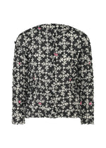 The SUIT MERINGUE TOP by me ISSEY MIYAKE is a long-sleeve, semi-sheer black blouse with white floral patterns, subtle pink accents, and a crushed pleat finish for added texture and elegance. - BLACK-HUED (no.18)