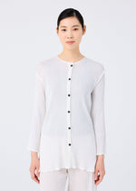 A woman faces forward against a plain light background, wearing the me ISSEY MIYAKE SEE-THROUGH CREPE COLOR— a white, long-sleeved cardigan with black buttons and matching white pants.