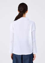 A woman with long dark hair in a low ponytail is seen from behind, wearing me ISSEY MIYAKE’s KNIT LIKE CLOTH white cotton-blend cardigan and dark blue pants—ideal for spring and summer—against a simple light background.
