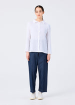Someone faces forward wearing the KNIT LIKE CLOTH white button-up shirt and loose dark blue trousers by me ISSEY MIYAKE, paired with white shoes against a light background—an ideal spring and summer look.