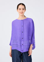A woman in a loose, textured purple SHEER SEE-THROUGH CREPE blouse by me ISSEY MIYAKE with front buttons and sheer hem panels pairs it with dark wide-leg pants, standing against a plain light background.