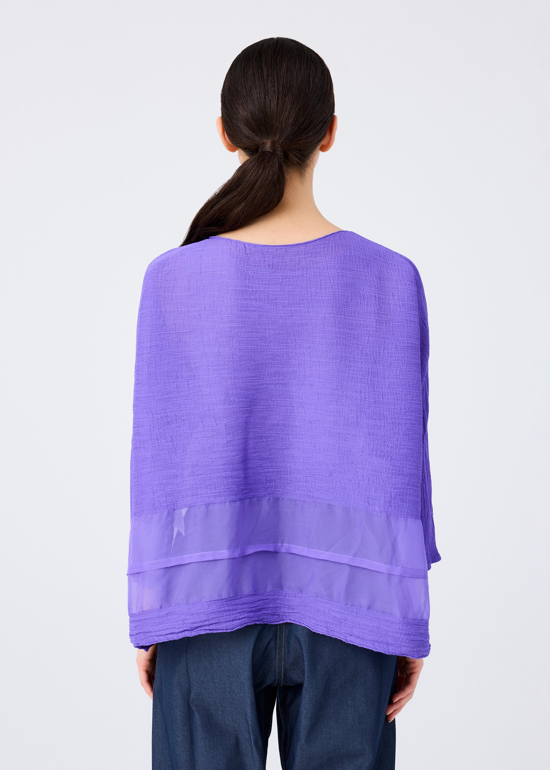 Zoomed view A person with long dark hair in a low ponytail is shown from behind, wearing the me ISSEY MIYAKE SHEER SEE-THROUGH CREPE top in textured purple with a sheer band and dark blue pants, set against a plain white background.