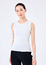 A woman with dark hair tied back wears a me ISSEY MIYAKE CAULIFLOWER round-neck sleeveless cotton top and black pinstriped pants, standing against a plain white background and looking at the camera with a slight smile.