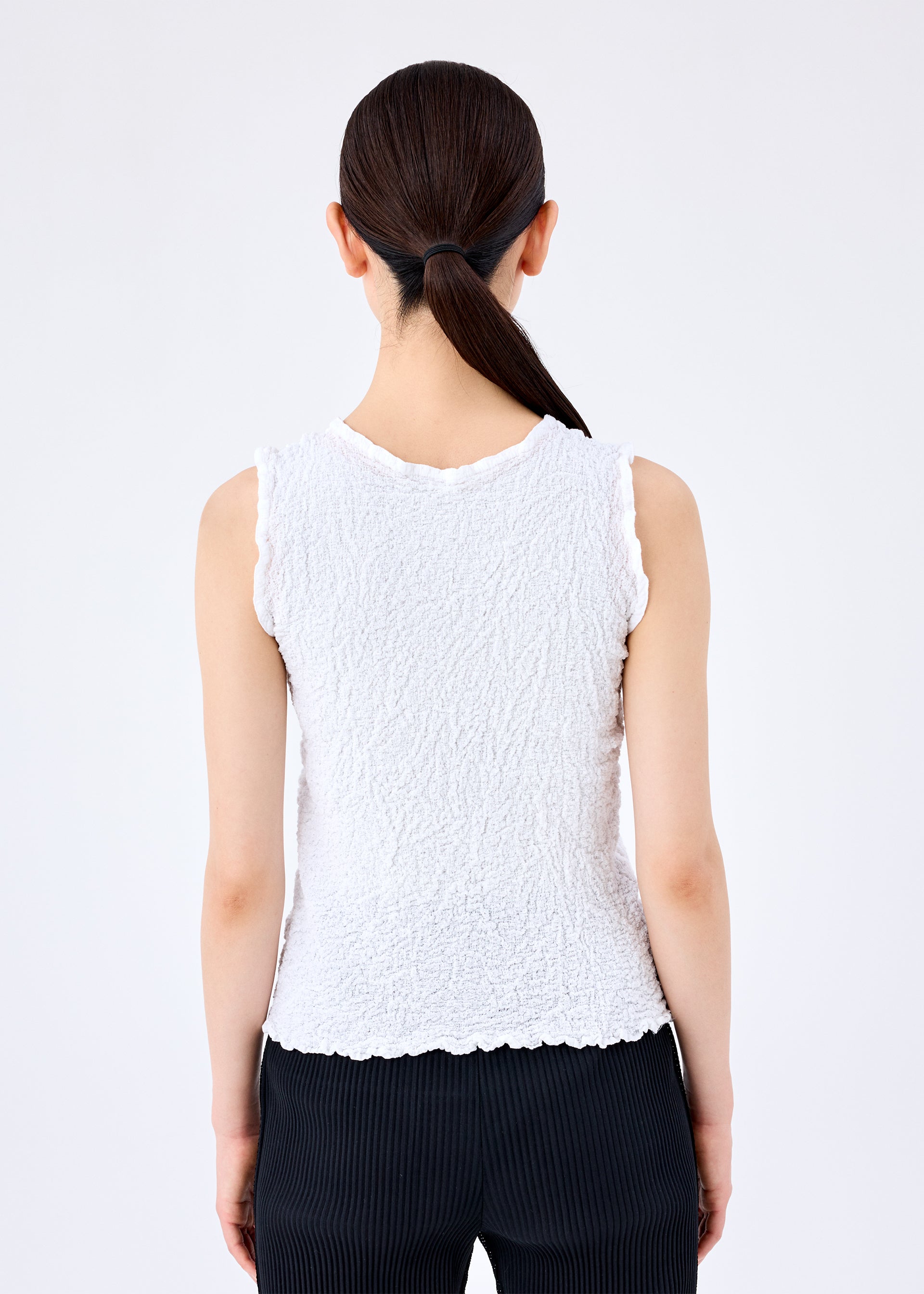 Zoomed view A person with straight dark hair in a low ponytail is shown from the back, wearing the CAULIFLOWER sleeveless cotton top and black pinstriped pants by me ISSEY MIYAKE against a plain light background.