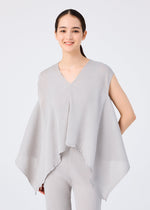 A young woman with long dark hair in a ponytail wears the me ISSEY MIYAKE FLAT SEE-THROUGH CREPE—a loose, sleeveless light gray top with wide sides over matching pants—standing against a plain white background and smiling gently.