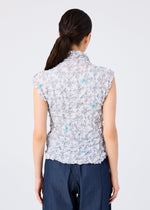 A person with long dark hair in a low ponytail is seen from the back, wearing the me ISSEY MIYAKE SUIT MERINGUE TOP with blue accents and a pleated finish, paired with dark blue pants against a plain light background.