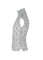 The SUIT MERINGUE TOP by me ISSEY MIYAKE, shown in light gray with a crushed pleat finish and subtle blue floral accents, is displayed in soft ruffles against a white background.