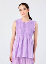A young woman with long dark hair in a low ponytail wears the SHIRT STRIPE CAULIFLOWER top by me ISSEY MIYAKE, standing against a light gray background and smiling gently at the camera.