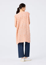 A woman stands facing away, wearing the me ISSEY MIYAKE SURPRISE BOX PRINT CAULIFLOWER peach tunic over dark blue wide-leg jeans and white slip-ons. Her dark hair is tied back in a low ponytail against a plain white background.