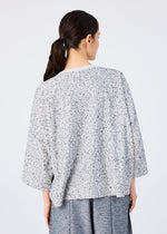 A woman with dark hair in a low ponytail is seen from behind, wearing the me ISSEY MIYAKE REmeTEX NEP JERSEY—a loose, light gray speckled sweater with wide sleeves—paired with gray pants against a plain light background.