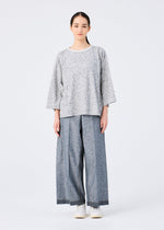 A woman with straight dark hair pulled back wears a me ISSEY MIYAKE REmeTEX NEP JERSEY light gray patterned top with wide sleeves and light blue-gray wide-leg pants, paired with white shoes, all set against a plain white background.