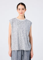 A young woman with long dark hair pulled back smiles gently at the camera, wearing the me ISSEY MIYAKE REmeTEX NEP JERSEY sleeveless top and loose gray pants, standing against a plain white background.