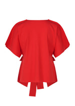 The FLAT JERSEY by me ISSEY MIYAKE is a red cotton-blend short-sleeve top with a wide neckline, loose fit, and decorative back fabric ties, shown on a plain white backdrop.