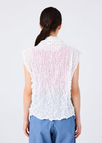 A person with long dark hair in a low ponytail is shown from the back, wearing the KALEIDOSCOPE LACE MERINGUE top by me ISSEY MIYAKE and blue pants against a plain white background.