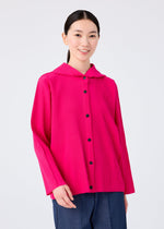 A woman with long dark hair smiles while wearing me ISSEY MIYAKE’s FINE KNIT PLEATS COLOR 1—a bright pink pleated knit button-up with black buttons and wide sleeves—paired with dark blue pants against a plain light background.