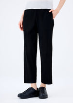 Model wears the FINE KNIT PLEATS BLACK pants by me ISSEY MIYAKE with black slip-on shoes and a white top; photo cropped waist down on a plain white background.