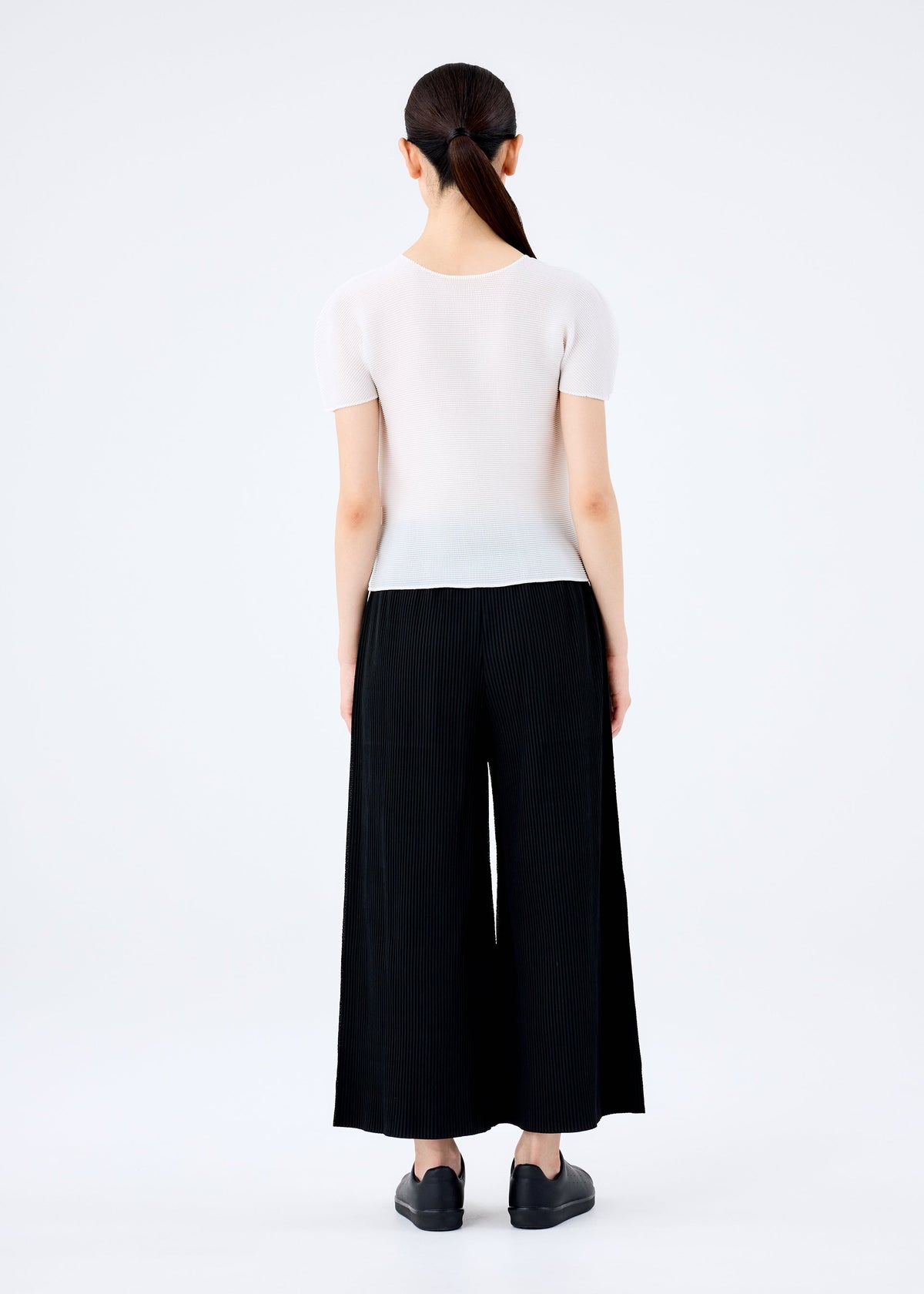 A woman wearing the FINE KNIT PLEATS BLACK wide pants by me ISSEY MIYAKE and a white shirt. view 4 of 5