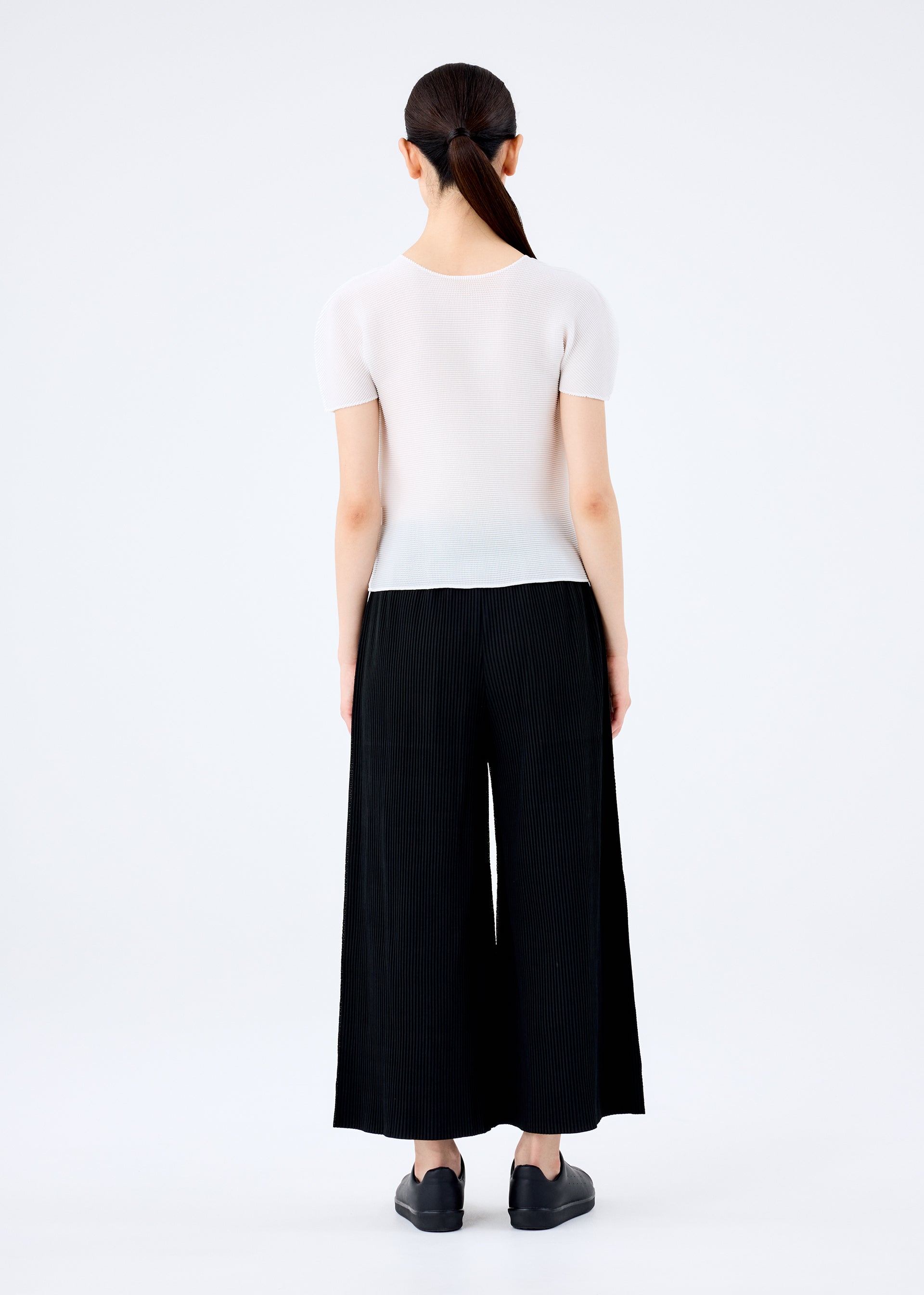 Zoomed view A woman wearing the FINE KNIT PLEATS BLACK wide pants by me ISSEY MIYAKE and a white shirt.