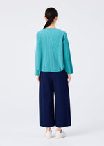 A person with long dark hair models the me ISSEY MIYAKE FINE KNIT PLEATS BOTTOM 1 wide-leg navy blue pants, paired with a teal knit top and white shoes, standing against a plain white background, facing away.