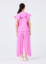 A woman with long dark hair in a ponytail faces away, wearing the me ISSEY MIYAKE TRICK PLEATS set—loose pink sleeveless top with large collar and matching wide-leg fine knit pleated pants—paired with white slip-ons, posed against a plain light background.
