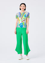 A woman stands smiling against a plain white background, wearing bright green FINE KNIT PLEATS BOTTOM 2 pants by me ISSEY MIYAKE, a colorful abstract print top, and white shoes.
