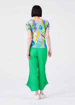 A person with short black hair stands facing away, wearing a colorful abstract top and bright green FINE KNIT PLEATS BOTTOM 2 pants by me ISSEY MIYAKE, paired with white shoes, on a plain light background.