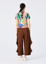 A person with long dark hair in a low ponytail wears a colorful short-sleeve top and the me ISSEY MIYAKE FINE KNIT PLEATS BOTTOM 2 pants with wavy side cutouts, standing against a plain white background, facing away.