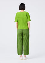 A person with short black hair stands facing away, wearing a bright green top, me ISSEY MIYAKE MIX FINE KNIT PLEATS BOTTOM pants in matching green, and white shoes against a plain white background.