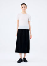 A woman stands against a white background, wearing the me ISSEY MIYAKE FINE KNIT PLEATS BLACK skirt paired with a short-sleeve white top and matching shoes. She faces forward with a neutral expression, her hair pulled back.