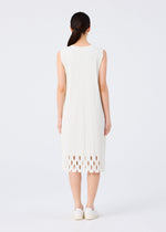 A woman with long dark hair in a low ponytail, facing away, wears the me ISSEY MIYAKE APERTURE PLEATS sleeveless knee-length pleated dress with a cutout hem and white shoes, standing against a plain white background.