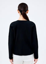 A person with long dark hair in a low ponytail stands facing away, wearing the me ISSEY MIYAKE FINE KNIT PLEATS BLACK top and white pants against a plain white background.