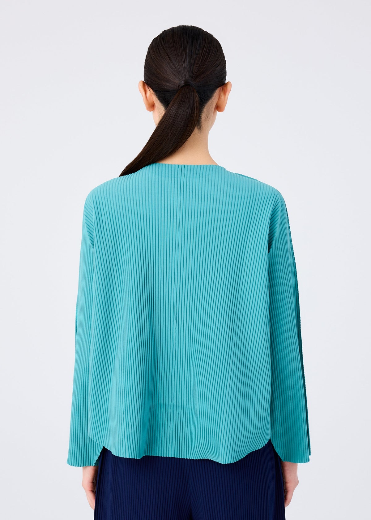 A person with long dark hair in a low ponytail is seen from the back, wearing the me ISSEY MIYAKE AURORA PLEATS teal knit cardigan and dark pants against a plain white background. view 7 of 8