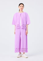 A woman with straight dark hair and white shoes wears the APERTURE PLEATS set by me ISSEY MIYAKE: a matching light purple pleated knit top and wide-leg pants with oval cut-out hems, standing against a plain white background.