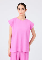 A woman with straight, dark hair pulled back wears the me ISSEY MIYAKE TRICK PLEATS set— a loose-fitting, fine knit pleats top with French sleeves and matching wide-leg pants—against a plain background, her expression neutral.