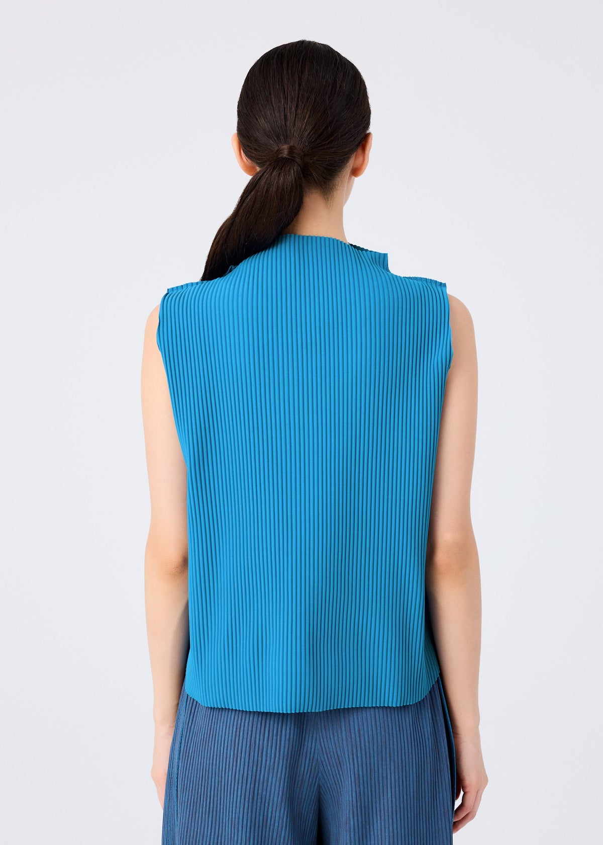 A person with long dark hair in a low ponytail is seen from behind, wearing the ROUND PLEATS sleeveless blue knit top and matching pants by me ISSEY MIYAKE, set against a plain light background. view 6 of 7