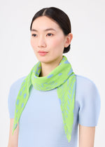 A woman with straight dark hair in a low bun wears the STARFISH PLEATS STOLE by me ISSEY MIYAKE, a lime green pleated accessory with blue polka dots, over a light blue textured top against a plain white background.