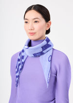 A woman with straight dark hair in a low bun stands against a plain white background, wearing a lavender textured top and the me ISSEY MIYAKE PLANT PLEATS STOLE with a plant pattern draped around her neck.