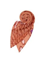 The PLANT PLEATS STOLE by me ISSEY MIYAKE features abstract plant patterns in orange and brown tones, with one end neatly rolled and the other end pointed, showcased against a white background.