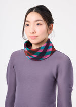 A woman in a textured purple top and the TAPE CHECK PLEATS STOLE by me ISSEY MIYAKE, featuring colorful stripes, stands against a white background, gazing slightly to the side with a neutral expression.