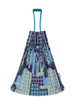 The BUILDING TRUNK PLEATS BAG by me ISSEY MIYAKE is a reusable tote featuring blue handles and a vibrant printed pattern with a cityscape and forest motif in shades of blue, green, and purple—perfect for urban farming adventures or everyday errands.