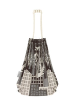 The BUILDING TRUNK PLEATS BAG by me ISSEY MIYAKE is a pleated mini tote featuring cream handles and an abstract grayscale cityscape design. The distinctive handle enhances its sophistication, while a small white tag accents one side.