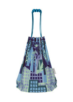 The BUILDING TRUNK PLEATS BAG by me ISSEY MIYAKE is a reusable mini tote in blue and purple, adorned with abstract geometric and nature-inspired patterns, featuring a distinctive wavy blue handle and a small white side tag.